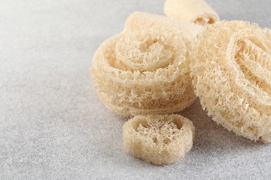 Photo of Different loofah sponges on light grey table, closeup. Space for text