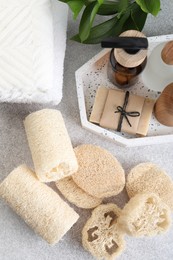Photo of Different loofah sponges, towels and cosmetic products on light grey table, flat lay