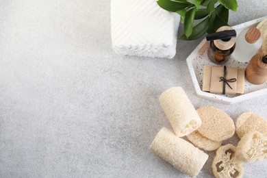 Photo of Different loofah sponges, towels and cosmetic products on light grey table, flat lay. Space for text