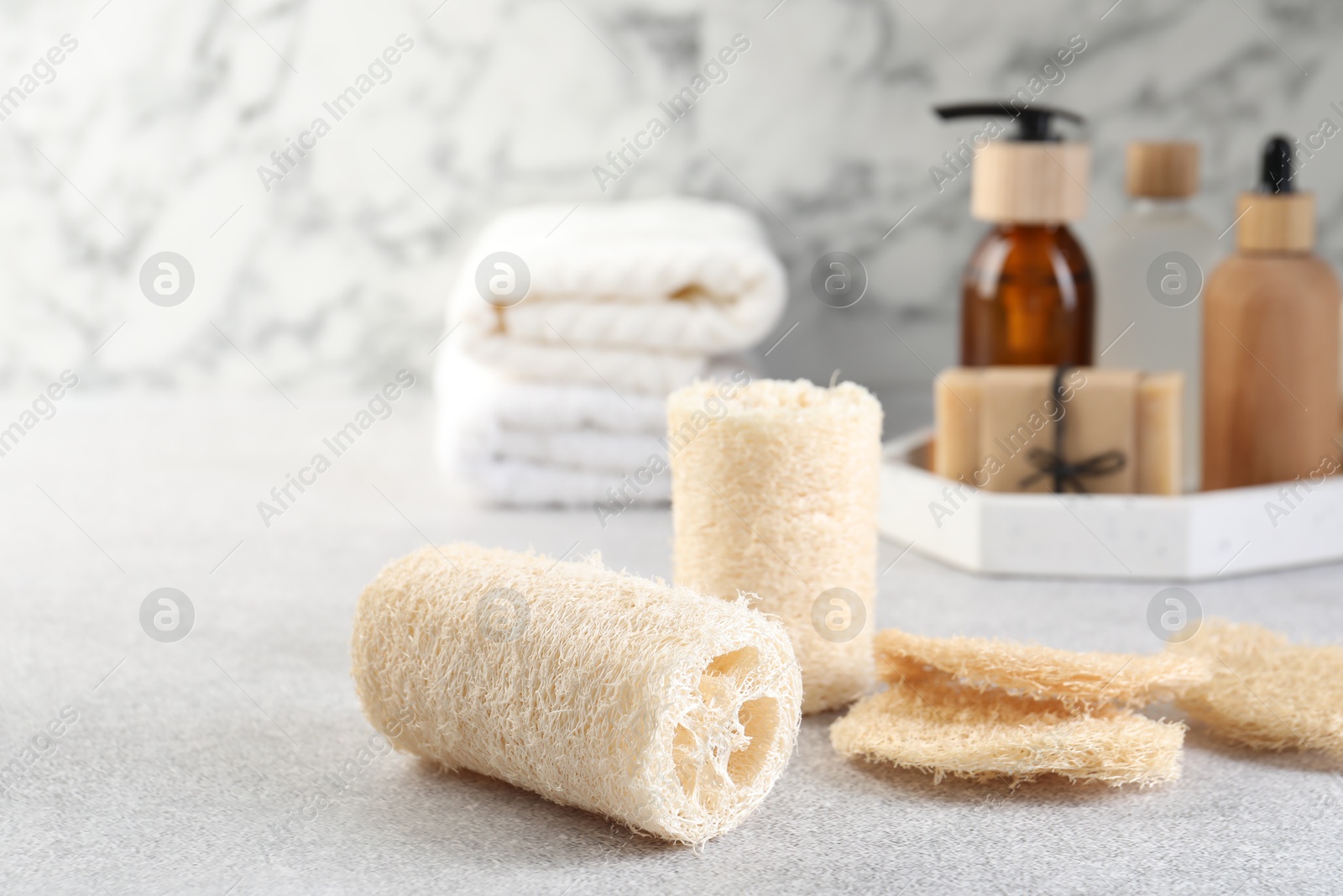 Different loofah sponges and cosmetic products on light grey table, closeup. Space for text Photo of Different loofah sponges and cosmetic products on light grey table, closeup. Space for text