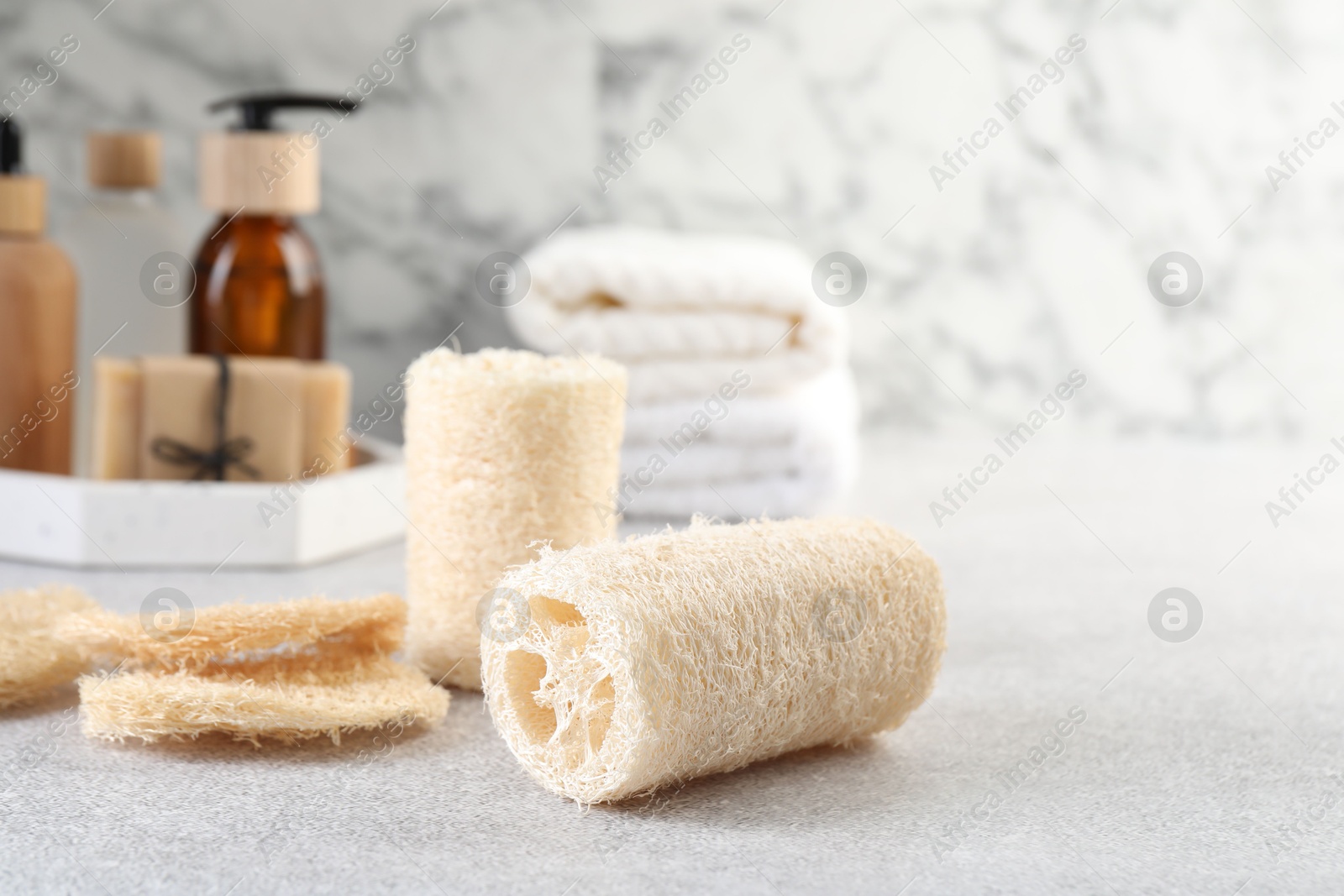 Different loofah sponges and cosmetic products on light grey table, closeup. Space for text Photo of Different loofah sponges and cosmetic products on light grey table, closeup. Space for text