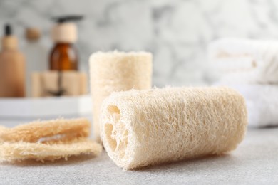 Photo of Different loofah sponges and cosmetic products on light grey table, closeup