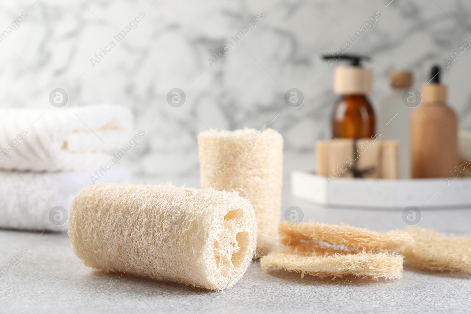 Different loofah sponges and cosmetic products on light grey table, closeup Photo of Different loofah sponges and cosmetic products on light grey table, closeup