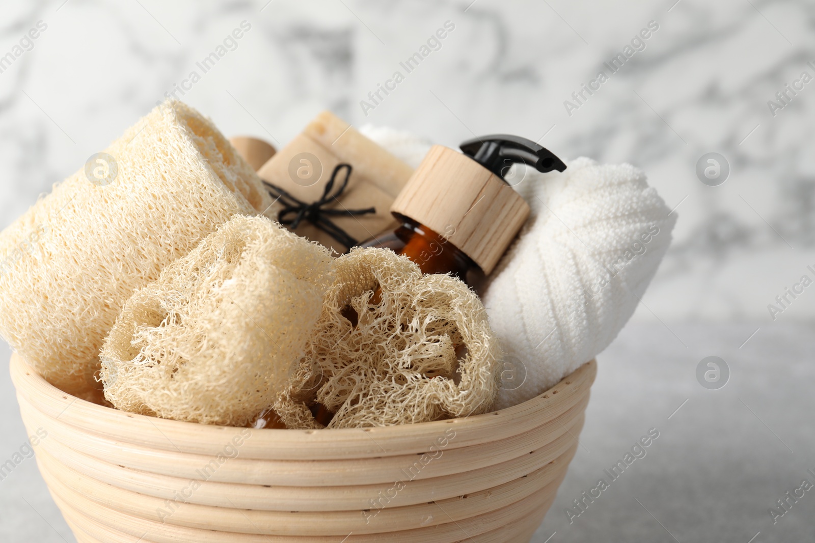Different loofah sponges, cosmetic products and towel in bowl on light grey table, closeup Photo of Different loofah sponges, cosmetic products and towel in bowl on light grey table, closeup