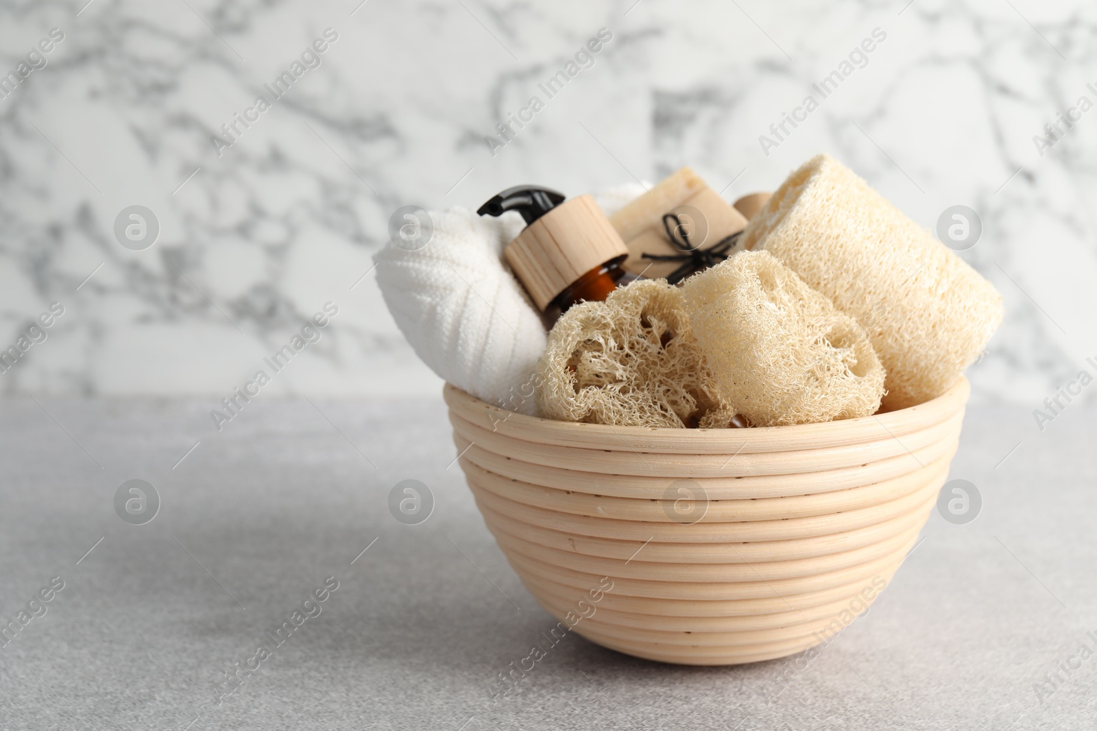 Different loofah sponges, cosmetic products and towel in bowl on light grey table, closeup. Space for text Photo of Different loofah sponges, cosmetic products and towel in bowl on light grey table, closeup. Space for text