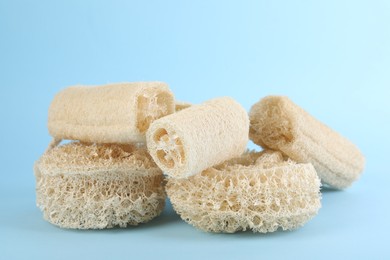 Photo of Different loofah sponges on light blue background, closeup