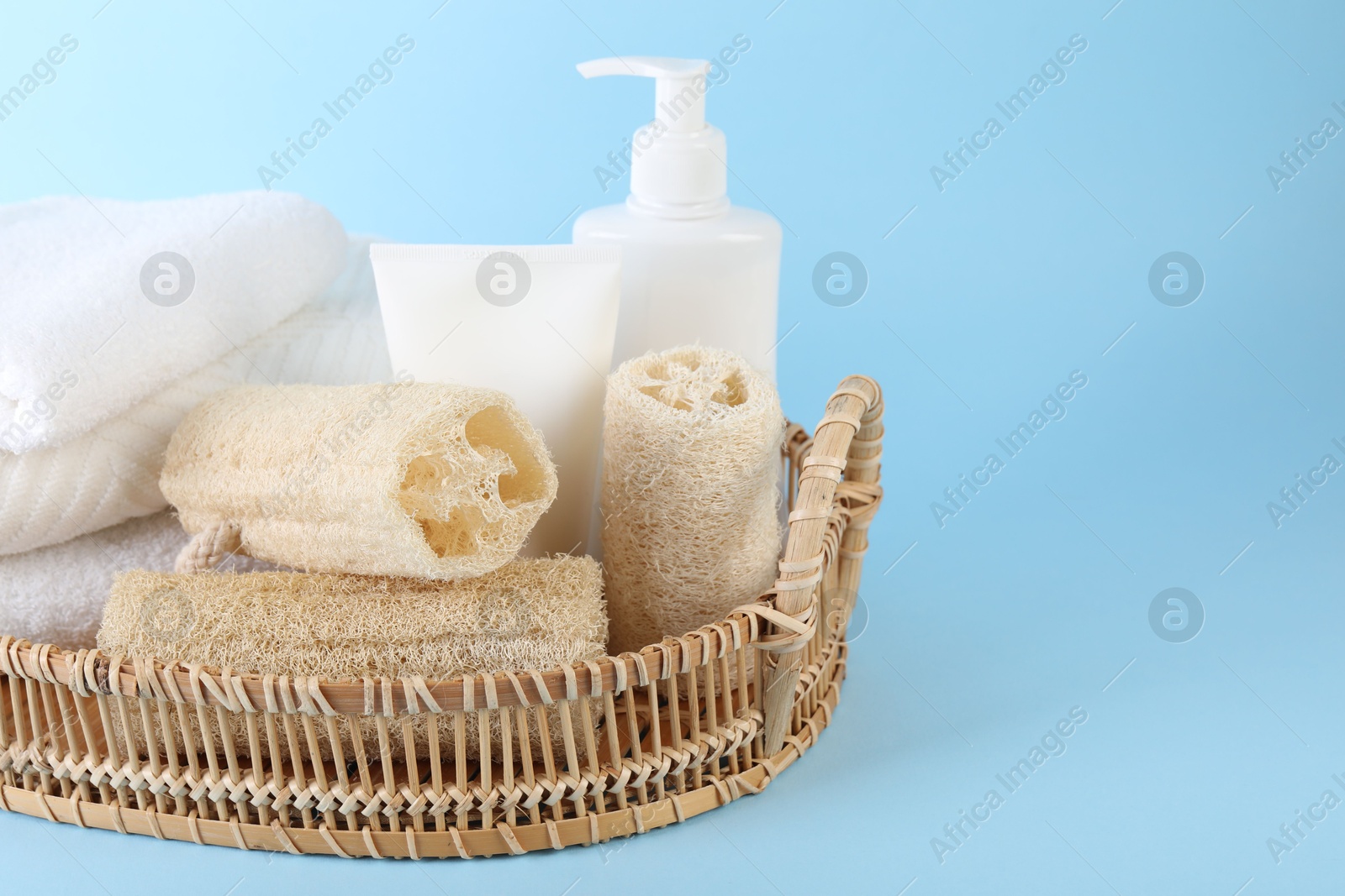 Different loofah sponges, cosmetic products and towels in wicker basket on light blue background, closeup. Space for text Photo of Different loofah sponges, cosmetic products and towels in wicker basket on light blue background, closeup. Space for text