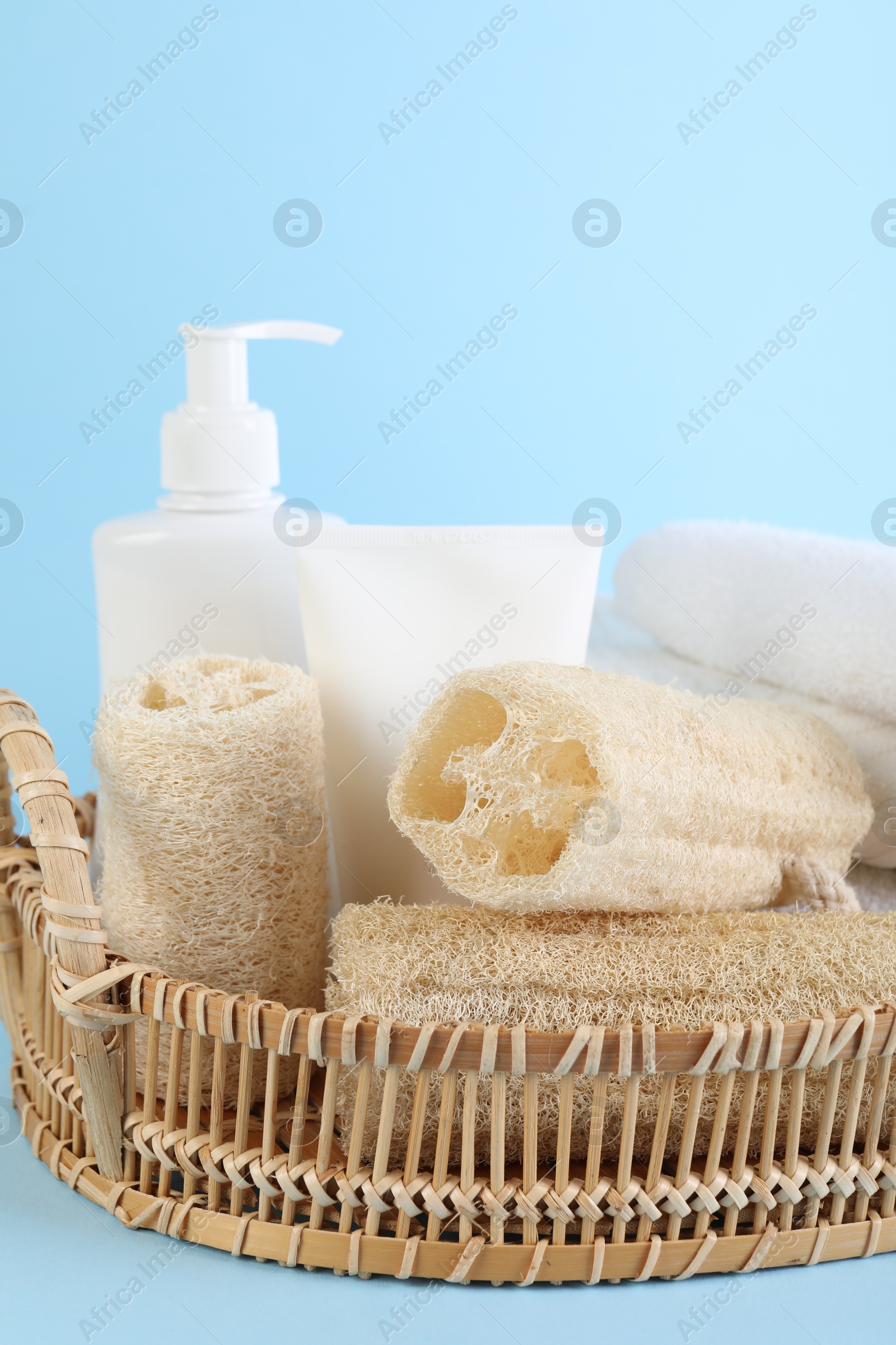 Different loofah sponges, cosmetic products and towels in wicker basket on light blue background, closeup Photo of Different loofah sponges, cosmetic products and towels in wicker basket on light blue background, closeup