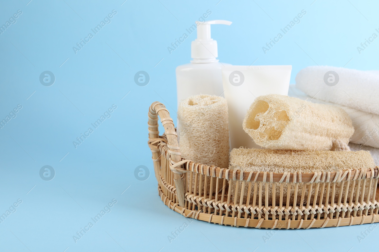 Different loofah sponges, cosmetic products and towels in wicker basket on light blue background, closeup. Space for text Photo of Different loofah sponges, cosmetic products and towels in wicker basket on light blue background, closeup. Space for text