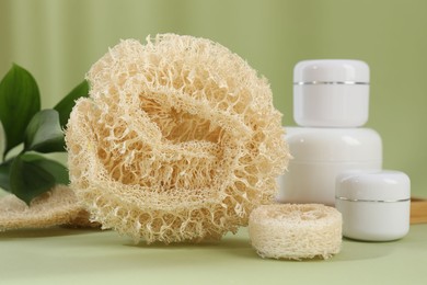 Photo of Loofah sponges and jars of cosmetic product on olive background, closeup