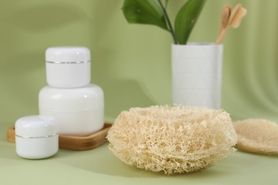 Photo of Loofah sponge and jars of cosmetic product on olive background, closeup