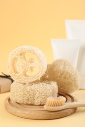Photo of Loofah sponges, toothbrush, tubes of cosmetic product and soap on beige background, closeup