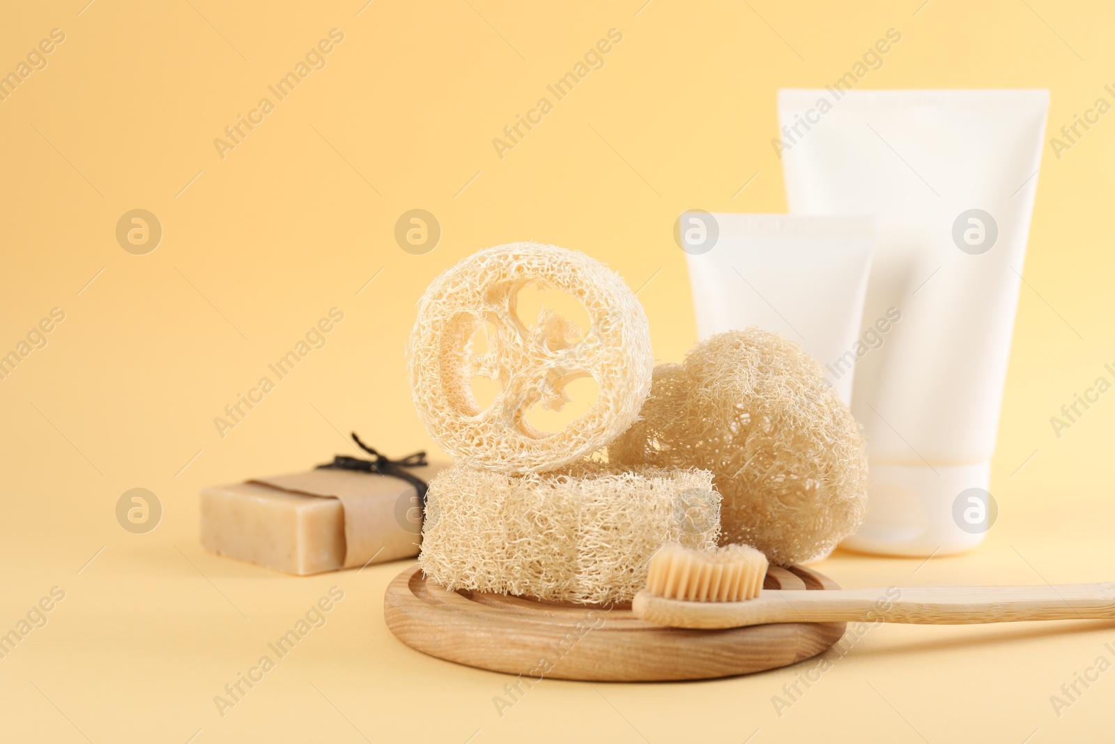 Loofah sponges, toothbrush, tubes of cosmetic product and soap on beige background, closeup. Space for text Photo of Loofah sponges, toothbrush, tubes of cosmetic product and soap on beige background, closeup. Space for text