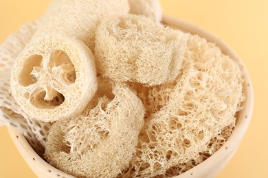 Photo of Different loofah sponges in bowl on beige background, closeup