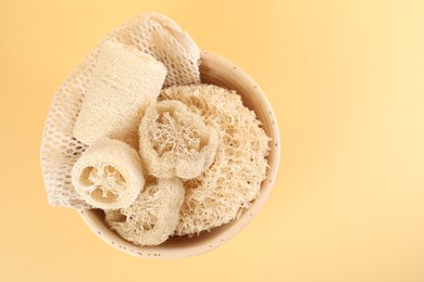Photo of Different loofah sponges in bowl on beige background, top view. Space for text