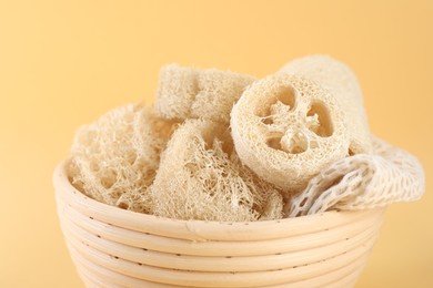 Photo of Different loofah sponges in bowl on beige background, closeup