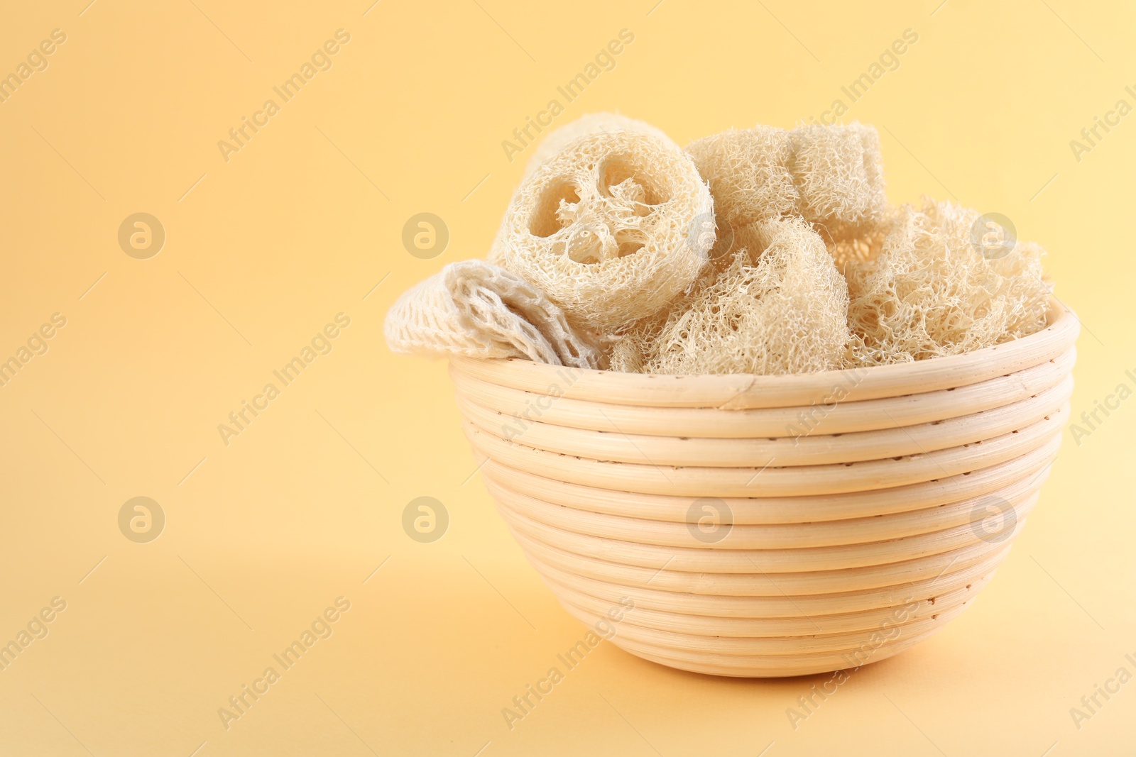 Different loofah sponges in bowl on beige background, closeup. Space for text Photo of Different loofah sponges in bowl on beige background, closeup. Space for text