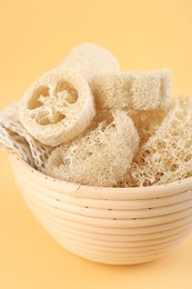 Photo of Different loofah sponges in bowl on beige background, closeup