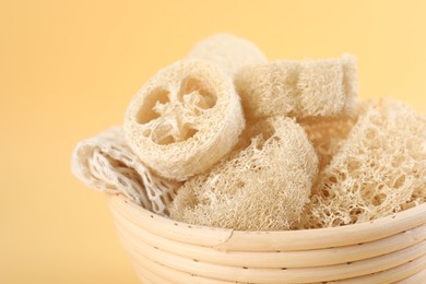 Photo of Different loofah sponges in bowl on beige background, closeup