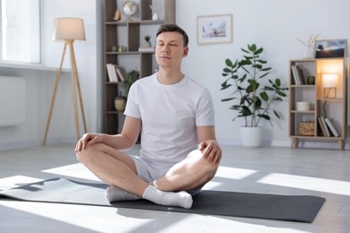 Photo of Young man practicing yoga on mat at home