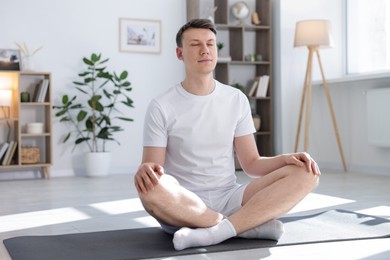 Photo of Young man practicing yoga on mat at home