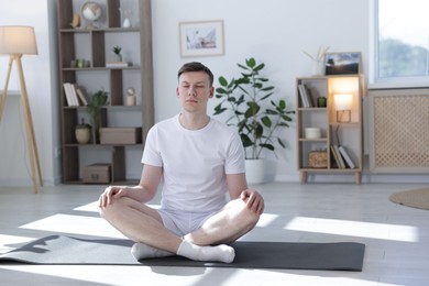 Photo of Young man practicing yoga on mat at home