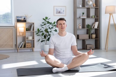 Photo of Young man practicing yoga on mat at home