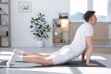 Photo of Young man practicing yoga on mat at home. Space for text