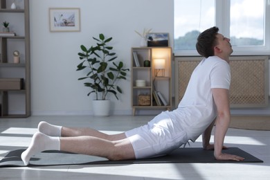 Photo of Young man practicing yoga on mat at home. Space for text