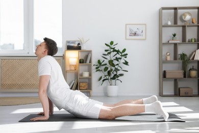 Photo of Young man practicing yoga on mat at home. Space for text
