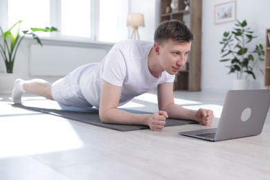 Photo of Man having online yoga class via laptop at home