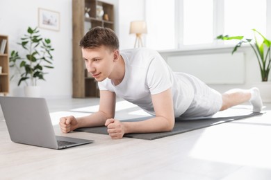 Photo of Man having online yoga class via laptop at home