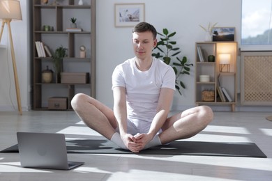 Photo of Man having online yoga class via laptop at home