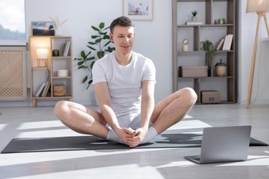 Photo of Man having online yoga class via laptop at home