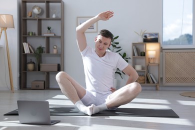 Photo of Man having online yoga class via laptop at home