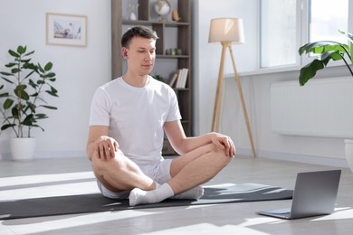 Photo of Man having online yoga class via laptop at home
