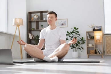 Photo of Man having online yoga class via laptop at home