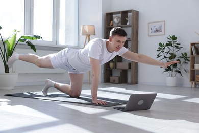 Photo of Man having online yoga class via laptop at home