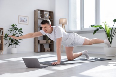 Photo of Man having online yoga class via laptop at home