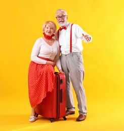 Photo of Lovely senior couple with suitcase on yellow background