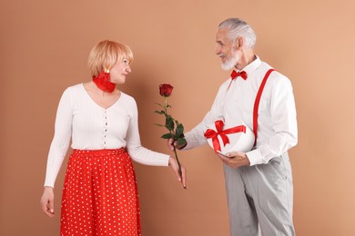 Photo of Lovely senior couple with gift box and rose on light brown background