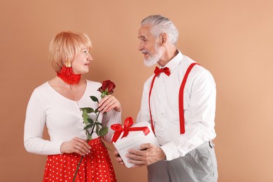 Photo of Lovely senior couple with gift box and rose on light brown background