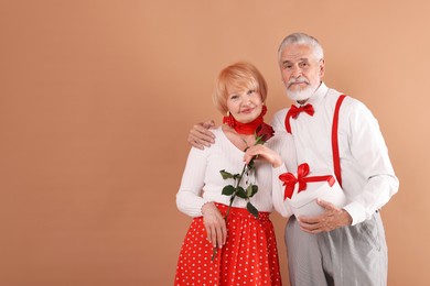 Photo of Lovely senior couple with gift box and rose on light brown background, space for text
