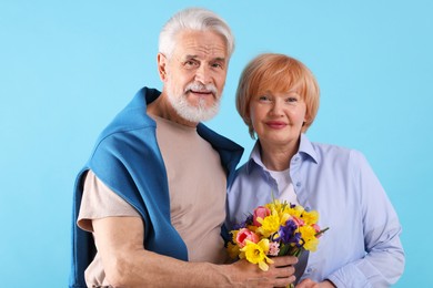 Photo of Lovely senior couple with bouquet of flowers on light blue background