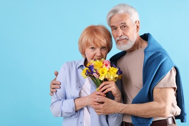 Photo of Lovely senior couple with bouquet of flowers on light blue background