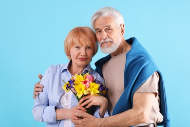 Photo of Lovely senior couple with bouquet of flowers on light blue background
