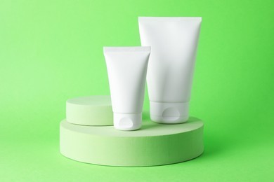 Photo of Stylish presentation of moisturizing body cream in tubes on light green background, closeup