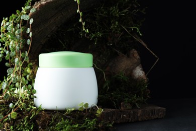 Photo of Jar of moisturizing body cream, tree bark and plants on grey table, closeup. Space for text