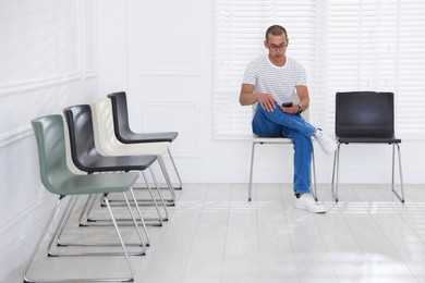 Photo of Man with smartphone waiting for appointment indoors
