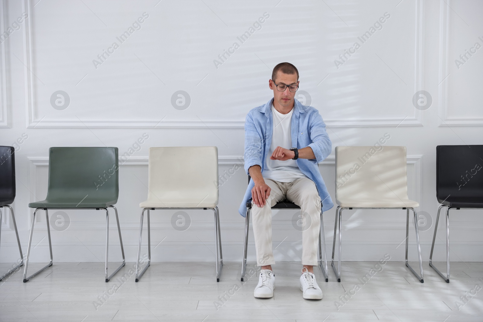 Man looking at wristwatch while waiting for appointment indoors Photo of Man looking at wristwatch while waiting for appointment indoors